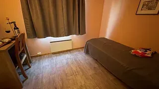 Enkeltrom med skrivebord, stol og seng med brunt sengeteppe i varmt belyst rom