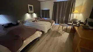 Stort rom med tre enkeltsenger, skrivebord og rolig stemningsbelysning