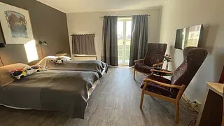 Rom med to enkeltsenger, godstoler og utgang til uteområde gjennom glassdør