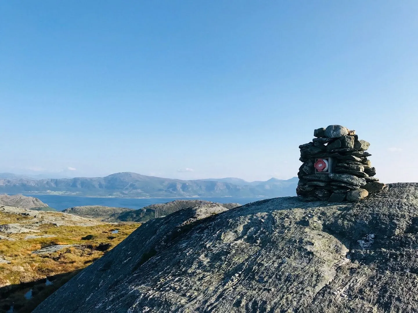 Varde av stein på fjelltopp med utsikt mot hav og fjell i klarvær